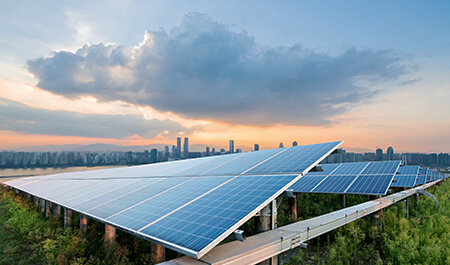 Solar panels facing sky at sunset with a city skyline in the background