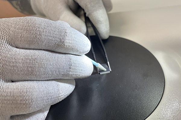 Close up of gloved lab technician's hands applying acetone dipped swab to the surface of a microchip